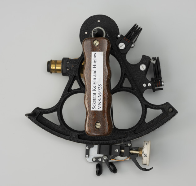Sekstant Kelvin & Hughes - ujęcie z tyłu; Sekstant z lunetką o długości od 7,2 do 10,5 cm. Sekstant zbudowany z czarnej, metalowej, odlewanej ramy w kształcie wycinka koła, łączonej wewnętrznie kratownicą w obrysie trójkąta o wymiarach : wysokość 10 centymetrów, długość umieszczonej osiowo ruchomej alidady 22,5 centymetra, promień limbusa 21,5 centymetrów, Alidada porusza się po wyskalowanym boku trójkąta – limbusie, wykonanym ze stali. Przy zakończeniu rozszerzenia znajduje się śruba zakończona bębenkiem z podziałką minutową z białego plastiku. Śruba ślimakowa zazębia się zębatką naciętą na krawędzi mosiężnej ramy. Naprzeciw małego lustra gwintowany uchwyt do mocowania lunetki, umożliwiający stabilne wkręcenie lunetki. W spodniej części drewniany, lakierowany uchwyt na dłoń i trzy nóżki stanowiące podstawę.