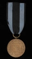 Medal Zasłużonym na Polu Chwały - ujęcie z tyłu; Rewers: na gładkim tle czworoboczna ramka obramowana wieńcem z liści laurowych; w ramce w czterech wierszach napis majuskułą ZASŁUŻONYM/NA POLU/CHWAŁY/1944. Medal zawieszony jest do czarnej wstążki z dwoma ciemnoniebieskim paskami.