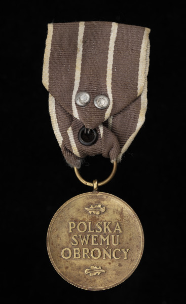 Medal Wojska - ujęcie z tyłu; Oznaka medalu okrągła z krawędziami obustronnie płasko podniesionymi. Na rewersie znajduje się napis: POLSKA / SWEMU / OBROŃCY; nad i pod napisem po jednym liściu dębowym. Wstążka jedwabna, wypłowiała, obecnie w kolorze brązowym (pierwotnie ciemnoczerwona), przedzielona dwoma paskami białymi pośrodku oraz białymi paskami na brzegach. Zapięcie na haftkę.