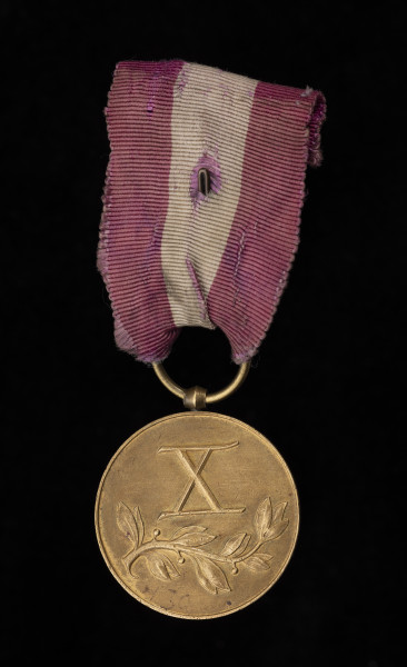 Medal Za Długoletnią Służbę III stopnia - rewers; kompozycja składająca się z wypukłej liczby rzymskiej „X”, poniżej której umiejscowiona jest gałązka wawrzynu. Zawieszenie z przylutowanego, beczułkowatego uszka i przewleczonego kółeczka. Wstążka z mory jedwabnej, amarantowa z białym pionowym pasem.