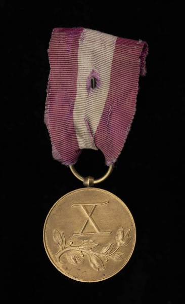 Medal Za Długoletnią Służbę III stopnia - rewers; kompozycja składająca się z wypukłej liczby rzymskiej „X”, poniżej której umiejscowiona jest gałązka wawrzynu. Zawieszenie z przylutowanego, beczułkowatego uszka i przewleczonego kółeczka. Wstążka z mory jedwabnej, amarantowa z białym pionowym pasem.
