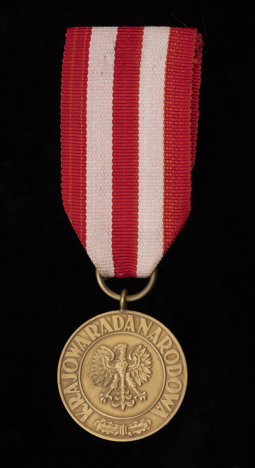 MNS/H/801 Medal Zwycięstwa i Wolności - Awers: w środku medalion z orłem państwowym (wzór z 1927 r. bez korony); w otoku napis majuskułą KRAJOWA RADA NARODOWA, pierwsze i trzecie słowo rozdzielone związanymi ze sobą liśćmi dębu z dwoma żołędziami. Zawieszenie z przylutowanego uszka i przewleczonego, zlutowanego kółeczka z gładkiego drutu. Wstążka z czerwonego rypsu.