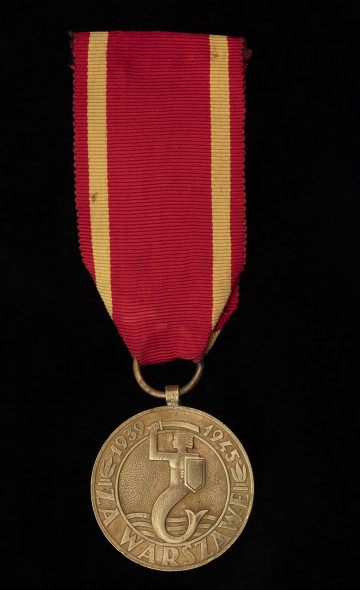 MNS/H/385 Medal za Warszawę 1939-1945 - ujęcie z przodu; Okrągły krążek, na którego awersie w środku wytłoczony jest wizerunek syreny z tarczą i mieczem (z herbu Warszawy), w dolnej części zaś trzy fale. Wizerunek Syreny otoczony jest pierścieniem, na którym w dolnej części umieszczony jest napis: ZA WARSZAWĘ, a w górnej części oddzielonej od dolnej zniczami umieszczone są daty: 1939 – 1945, pomiędzy którymi znajduje się miecz Syreny. Medal posiada czerwoną wstążkę z żółtymi paskami po bokach.