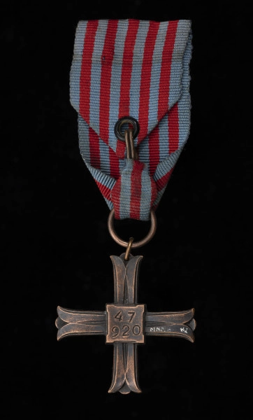Krzyż Pamiątkowy Monte Cassino - ujęcie z tyłu; Krzyż równoramienny w kształcie krzyża benedyktyńskiego, równoramiennego, o profilowanych ramionach. Na rewersie, także na tarczce, znajduje się wklęsły, wybity numer  w dwóch wierszach: 47 920 Zawieszenie z kółka przewleczonego przez przewiercone ramię krzyża, do niego doczepione większe kółko. Wstążka koloru jasnoniebieskiego z pięcioma paskami czerwono-pomarańczowymi przebiegającymi przez środek wstążki. Wstążka zapinana na haftkę.