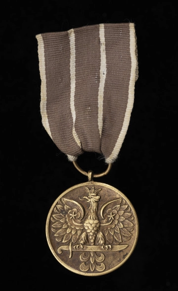 Medal Wojska - ujęcie z przodu; Oznaka medalu okrągła z krawędziami obustronnie płasko podniesionymi. Na awersie znajduje się stylizowany orzeł w koronie, siedzący na mieczu. Wstążka jedwabna, wypłowiała, obecnie w kolorze brązowym (pierwotnie ciemnoczerwona), przedzielona dwoma paskami białymi pośrodku oraz białymi paskami na brzegach.