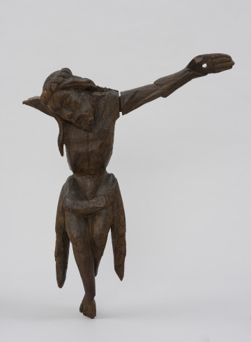 MNS/Szt/48 figura krucyfiksu - ujęcie z przodu; Sylwetka o krępej, geometrycznej budowie ukazana została frontalnie, w układzie symetrycznym, z głową opadającą na prawe ramię. Długie szczupłe ręce o dłoniach zwróconych wnętrzem układają się ukośnie do góry. Wypukły tors o zapadniętym brzuchu oddzielony od partii krągłych ud wąską talią. Biodra okrywa chusta ułożona w poziomy wałek, której końce opadają symetrycznie po bokach. Lekko podkurczone golenie skrzyżowane są prawa nad lewą. Twarz o krótkim zaroście skierowana jest do przodu. Oczy są zamknięte. Na głowie widoczna jest korona cierniowa w formie skręconego z dwóch splotów grubego sznura. Włosy opadają falistym pasmem na tors. Powierzchnia rzeźby jest uszkodzona. Brakuje prawego przedramienia Chrystusa. W koronie widoczne wgłębienia po cierniach, z których zachował się jeden. W dłoni i stopach duże otwory do mocowania na krzyżu.