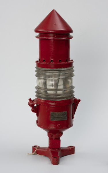 Latarnia torowa - ujęcie z tyłu; Czerwona latarnia gazowa, acetylenowa typu Lebe stosowana na znakach torowych pływających. Tabliczka znamionowa ze znakiem firmowym AGA system DALEN Gasaccumulator Stockholm. Korpus wykonany z blachy mosiężnej, pomalowany na kolor czerwony. Wbudowana soczewka Frensela wysokości 105 mm i średnicy 135 mm. Soczewka z kominem zamocowana do korpusu na zawiasie i blokowana śrubą. Komin średnicy 100 mm i wysokości 190 mm zakończony stożkiem. W dolnej części korpusu, w kostce o kształcie sześcianu otwór gwintowany służący do doprowadzenia gazu do palnika. Latarnia mocowana na trzy śruby do korpusu pławy, przez otwory znajdujące się w spodzie podstawy.