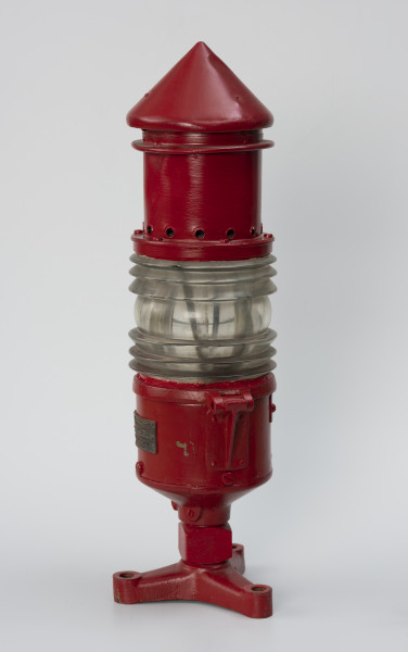 Latarnia torowa - ujęcie z boku; Czerwona latarnia gazowa, acetylenowa typu Lebe stosowana na znakach torowych pływających. Korpus wykonany z blachy mosiężnej, pomalowany na kolor czerwony. Wbudowana soczewka Frensela wysokości 105 mm i średnicy 135 mm. Soczewka z kominem zamocowana do korpusu na zawiasie i blokowana śrubą. Komin średnicy 100 mm i wysokości 190 mm zakończony stożkiem. W dolnej części korpusu, w kostce o kształcie sześcianu otwór gwintowany służący do doprowadzenia gazu do palnika. Latarnia mocowana na trzy śruby do korpusu pławy, przez otwory znajdujące się w spodzie podstawy.
