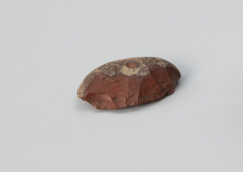 drapacz - Ujęcie z drugiego boku; Niewielki drapacz wykonany z łuszczki (formy odłupkowej) krzemienia pomorskiego (jaskółczy chlebek) na zewnątrz jest czerwony, a w środku biały.