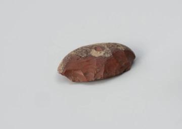 drapacz - Ujęcie z drugiego boku; Niewielki drapacz wykonany z łuszczki (formy odłupkowej) krzemienia pomorskiego (jaskółczy chlebek) na zewnątrz jest czerwony, a w środku biały.