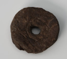 pływak - Ujęcie z góry; Pływak wykonano z kawałka kory drzewa iglastego. Zabytek kształtem zbliżony jest do nieregularnego koła. W środku przedmiotu znajduje się otwór przelotowy. Na powierzchni znajdują się widoczne ślady obróbki wykonanej za pomocą ostrego noża.