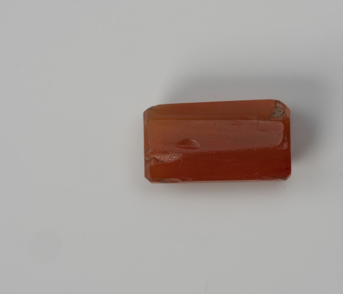 Paciorek wielościenny - ujęcie z boku; Paciorek z karneolu w kształcie wydłużonego prostopadłościanu, w przekroju ośmioboczny.