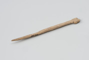 szpila kościana do spinania włosów lub szat - Ujęcie ze skosu z prawej; Ozdobna szpila wykonana z kości zwierzęcej. Z jednej strony ma zaostrzoną końcówkę, z drugiej natomiast zakończona była płaskim zgrubieniem o nieregularnym kształcie (teraz ułamanym).