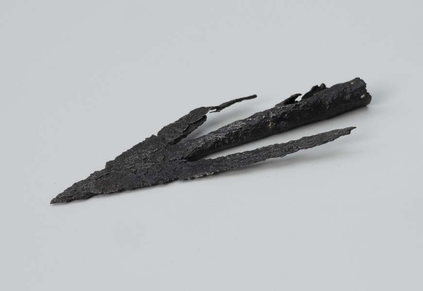 Grot strzały łuku - ujęcie z przodu od prawej; Żelazny grot strzały łuku charakteryzuje się długimi zadziorami liścia i stożkowatą tulejką do osadzenia na drzewcu.