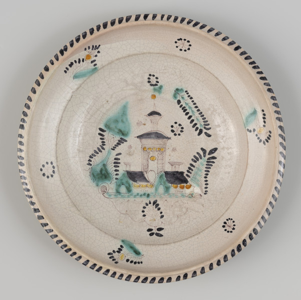 talerz - Ujęcie z góry; Talerz z czarą naczynia stosunkowo płaską obwiedzioną wyraźnie zaznaczonym wylewem z wysokim rantem i kołnierzem. Szkliwo ołowiowo-cynowe w tonacji szarej pokrywa tylko wewnętrzną stronę i stanowi tło dla odręcznej dekoracji wykonanej tlenkami miedzi, manganu, chromu i antymonu. Trójbarwny, czarno-zielono-żółty malunek przedstawia trzyczęściową budowlę z wieżą, pod którą znajduje się słabo widoczna data z cyframi przedzielonymi stylizowanym koszem z kwiatami. Wokół budowli dekoracja o motywach roślinnych. Wylew zdobiony powtarzającymi się trzykrotnie naprzemiennie wzorami kwiatowymi realistycznymi i schematycznymi. Kołnierz dekorowany skośnymi kreskami. W górnej części wylewu, nad budowlą, wyraźnie cieńsza powłoka szkliwa.