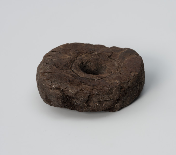 pływak - Ujęcie góry od przodu; Pływak wykonano z kawałka kory drzewa iglastego. Zabytek kształtem zbliżony jest do nieregularnego koła. W środku przedmiotu znajduje się otwór przelotowy. Na powierzchni znajdują się widoczne ślady obróbki wykonanej za pomocą ostrego noża.