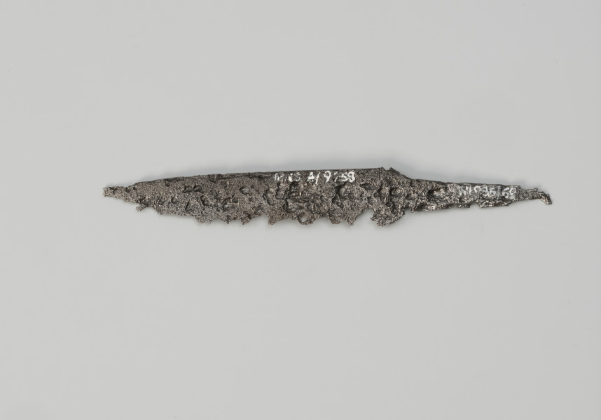 nóż - Ujęcie z tyłu; Niewielkich rozmiarów nóż żelazny charakteryzujący się wąską głownią, prostym tylcem z lekko łukowatym ostrzem oraz trzpieniem wyodrębnionym dwustronnie. Rękojeść niezachowana.