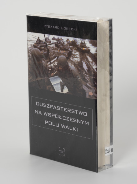 Ryszard Górecki. Duszpasterstwo na współczesnym polu walki - ujęcie z przodu; Obłożony w foliową koszulkę obiekt-książka. Na frontowej stronie czarnej okładki okładce od góry białe napisy: nazwisko autora (RYSZARD GÓRECKI), fotografia z pola bitwy (na pierwszym planie dwaj żołnierze czytający Biblię, w tle kawalkada czołgów sunących przez rozmokłe, częściowo zaśnieżone pole), poniżej zdjęcia: tytuł publikacji (DUSZPASTERSTWO NA WSPÓŁCZESNYM POLU WALKI) i logo wydawnictwa Niewidzialny Znak.