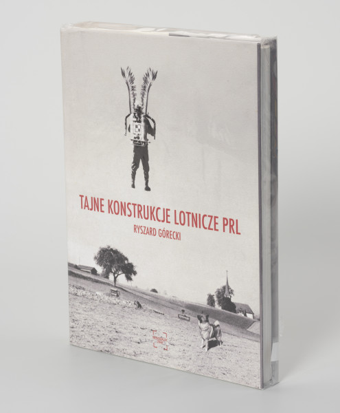 Ryszard Górecki. Tajne konstrukcje lotnicze PRL - ujęcie z przodu; Obłożony w foliową koszulkę obiekt-książka. Na frontowej stronie okładki czarno-biały fotomontaż z przedstawieniem odwróconego tyłem, unoszącego się w powietrzu żołnierza. Na plecach żołnierza plecak odrzutowy oznakowany szachownicą (symbolem polskich lotniczych sił zbrojnych), na ramionach skrzydła polskiej husarii. Żołnierz unosi się nad zaoranymi polami. Na pierwszym planie po prawej stronie pies, w tle po  prawej sylweta kościoła, po lewej zabudowania gospodarcze. Na środku okładki czerwony napis z tytułem publikacji (TAJNE KONSTRUKCJE LOTNICZE PRL) i nazwiskiem autora (RYSZARD GÓRECKI). U dołu okładki czerwone logo wydawnictwa Niewidzialny Znak.