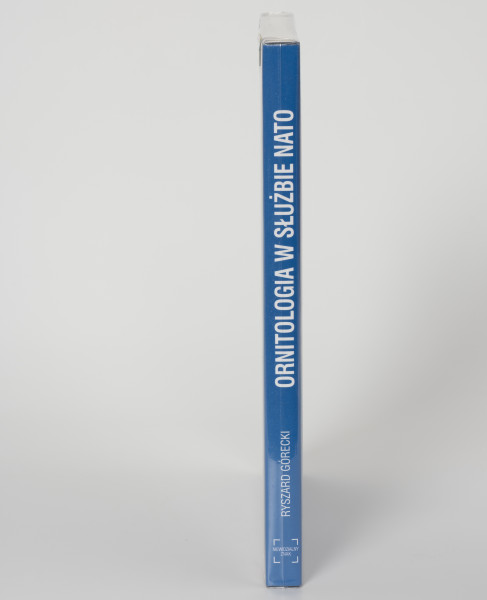 Ryszard Górecki. Ornitologia w służbie NATO - ujęcie z przodu; Obłożony w foliową koszulkę obiekt-książka. Na grzbiecie od góry białymi literami tytuł publikacji, nazwisko autora, logo wydawnictwa. logo, nazwisko autora i tytuł.