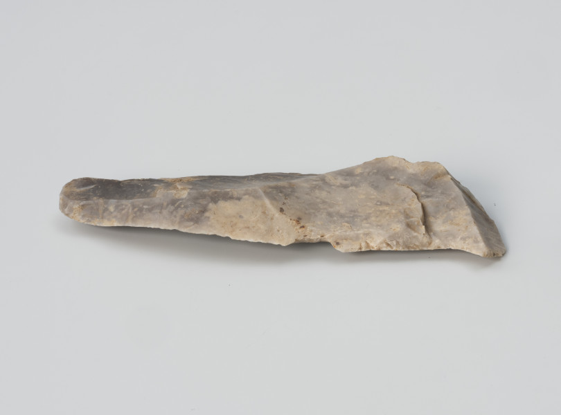 przekłuwacz typu Zinken - Ujęcie z drugiego boku; Duży przekłuwacz typu Zinken wykonany na nieregularnym wiórze z negatywami zaprawy oraz fragmentami kory widocznymi na stronie wierzchniej. Z lewej strony zakończony jest grubym wierzchołkiem, stanowiącym część pracującą, tzw. żądło, uformowane drobnym retuszem. Na krawędzi wióra widoczne są ślady retuszu użytkowego.