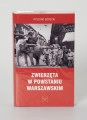 Ryszard Górecki. Zwierzęta w Powstaniu Warszawskim - ujęcie z przodu; Obłożony w foliową koszulkę obiekt-książka. Na frontowej stronie czerwonej okładki od góry: białymi literami nazwisko autora (RYSZARD GÓRECKI), poniżej fotomontaż z przedstawieniem czarno-białej sceny z Powstania Warszawskiego (fragment ulicy przedstawionej w perspektywicznym skrócie, obie pierzeje ciasno zabudowane kilkupiętrowymi kamienicami, na pierwszym planie po prawej grupa uzbrojonych powstańców, po lewej słoń z koszem na grzbiecie, w koszu powstaniec z pistoletem i małpa z granatem, pod zdjęciem białymi literami: tytuł publikacji (ZWIERZĘTA W POWSTANIU WARSZAWSKIM) oraz logo wydawnictwa Niewidzialny Znak.