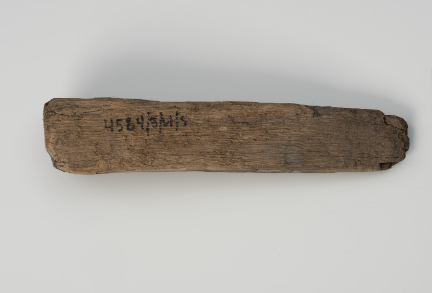 Klin - Ujęcie z dołu; Klin w formie graniastosłupa o przekroju zbliżonym do wydłużonego trójkąta równoramiennego. Powierzchnię pozostawiono nieobrobioną, surową i ze śladami cięcia piłą.