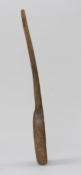 szufla do ziarna - Ujęcie z boku; Szufla do ziarna wykonana z jednego kawałka drewna. Część pracująca wąska i długa o wyraźnie podniesionych ściankach bocznych. Ścianki boczne w górnej partii łagodnie się zwężają i przechodzą w lekko wygięty i zakończony półokrągło trzonek o przekroju owalnym.