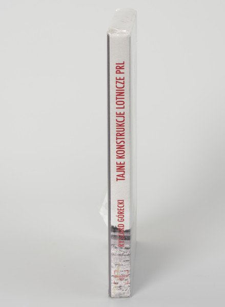 Ryszard Górecki. Tajne konstrukcje lotnicze PRL - ujęcie z boku; Obłożony w foliową koszulkę obiekt-książka. Na grzbiecie od góry: logo, tytuł publikacji, nazwisko autora i logo wydawnictwa.