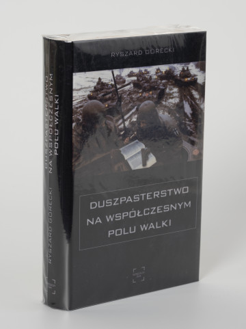 Ryszard Górecki. Duszpasterstwo na współczesnym polu walki - ujęcie z boku; Obłożony w foliową koszulkę obiekt-książka. Na frontowej stronie czarnej okładki okładce od góry białe napisy: nazwisko autora (RYSZARD GÓRECKI), fotografia z pola bitwy (na pierwszym planie dwaj żołnierze czytający Biblię, w tle kawalkada czołgów sunących przez rozmokłe, częściowo zaśnieżone pole), poniżej zdjęcia: tytuł publikacji (DUSZPASTERSTWO NA WSPÓŁCZESNYM POLU WALKI) i logo wydawnictwa Niewidzialny Znak. Na grzbiecie od góry: tytuł publikacji, nazwisko autora i logo wydawnictwa.