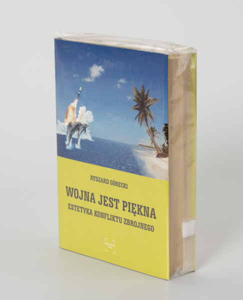 Ryszard Górecki. Wojna jest piękna. Estetyka konfliktu zbrojnego. - ujęcie z przodu; Obłożony w foliową koszulkę obiekt-książka. Okładka w kolorze limonkowym. Na frontowej stronie od góry: fotomontaż z przedstawieniem błękitnego morza i fragmentu egzotycznej piaszczystej plaży z palmami. Horyzont w 3/4 wysokości przedstawienia, partie nieba błękitne z kilkoma białymi pierzastymi chmurkami. Na pierwszym planie po lewej trzy wyskakujące z morza delfiny, za nimi wznoszący się w górę pocisk balistyczny, poniżej zdjęcia kolejno czarnymi literami: nazwisko autora (RYSZARD GÓRECKI) i tytuł publikacji (WOJNA JEST PIĘKNA. ESTETYKA KONFLIKTU ZBROJNEGO), u dołu okładki logo Wydawnictwa Niewidzialny Znak.