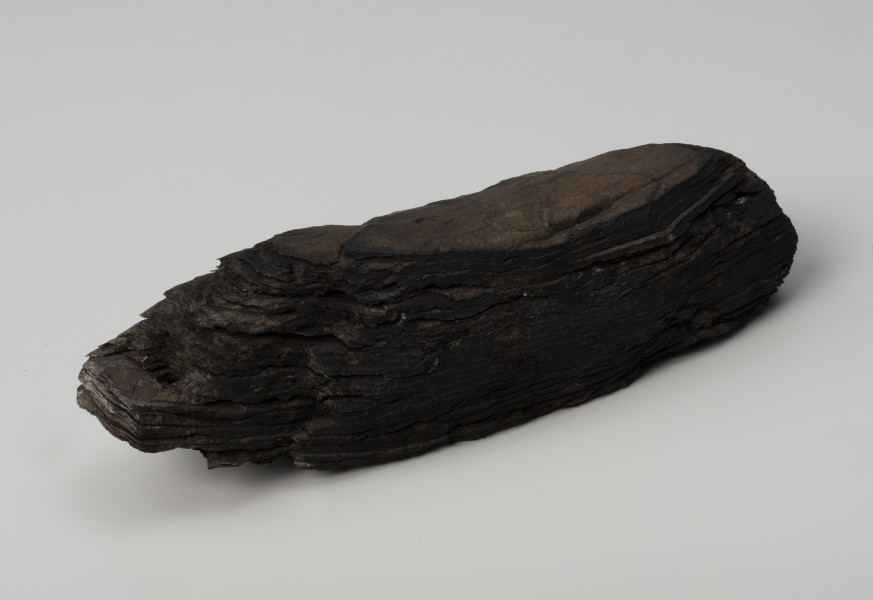 pływak do sieci - Ujęcie ze skosu z prawej góry; Pływak wykonany z jednego, dość dużego kawałka kory, najpewniej sosnowej. Posiada formę wydłużoną i zaopatrzony jest w słabo widoczne dwa otwory do przeciągania liny na lewym końcu.