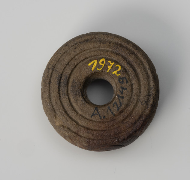 Przęślik - ujęcie z dołu; Krążkowy przęślik z miękkiego surowca skalnego, zdobiony motywem trzech dookolnych linii rytych na biegunie.