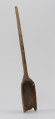szufla do ziarna - Ujęcie ze skosu z lewej; Szufla do ziarna wykonana z jednego kawałka drewna. Część pracująca wąska i długa, głęboko wyżłobiona o wyraźnie podniesionych ściankach bocznych. Ostrze łyżki uszkodzone mechanicznie, w dwóch miejscach ślady po sękach. Ścianki boczne w górnej partii łagodnie się zwężają i przechodzą w lekko wygięty i zakończony półokrągło trzonek o przekroju owalnym.