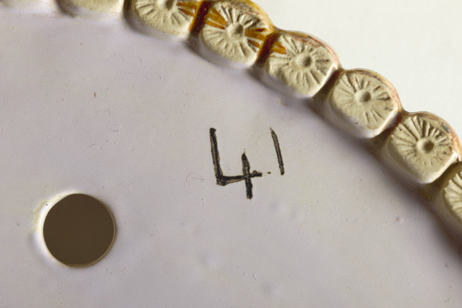 cache-pôt to duże naczynie cylindryczne, o grubych ściankach, z podstawką. Zewnętrzna powierzchnia ścianek modelowana jest na kształt wiązek łodyg bambusowych przewiązanych wstążką z kokardą. Łodygi malowane są naturalistycznie, w kolorze żółtym i brązowym. Donica i podstawka pokryte są wewnątrz polewą w kolorze liliowym. 