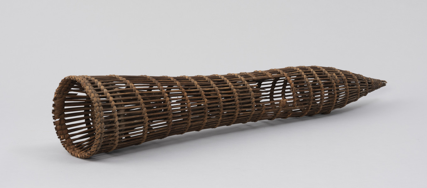 wiersza - Ujęcie ze skosu od tyłu; Wiersza wypleciona z wikliny o długim, prostym, cylindrycznym korpusie zakończonym stożkowato z prawej strony a okrągłym otworem z lewej. Wykonana z wiklinowych prętów ułożonych na trzech obręczach z cienkich patyków, które przepleciono spiralnie w kilkunastu miejscach łykiem. Wewnątrz dwa lejki stanowiące integralną całość z korpusem. W około połowie długości narzędzia wycięty prostokątny otwór, przez który wyjmowana byłą ryba. Pierwotnie najprawdopodobniej do otworu mocowane były drzwiczki.