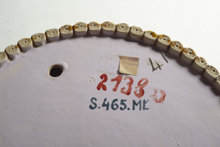 duże naczynie cylindryczne, o grubych ściankach, z podstawką. Zewnętrzna powierzchnia ścianek modelowana jest na kształt wiązek łodyg bambusowych przewiązanych wstążką z kokardą. Łodygi malowane są naturalistycznie, w kolorze żółtym i brązowym. Donica i podstawka pokryte są wewnątrz polewą w kolorze liliowym. 