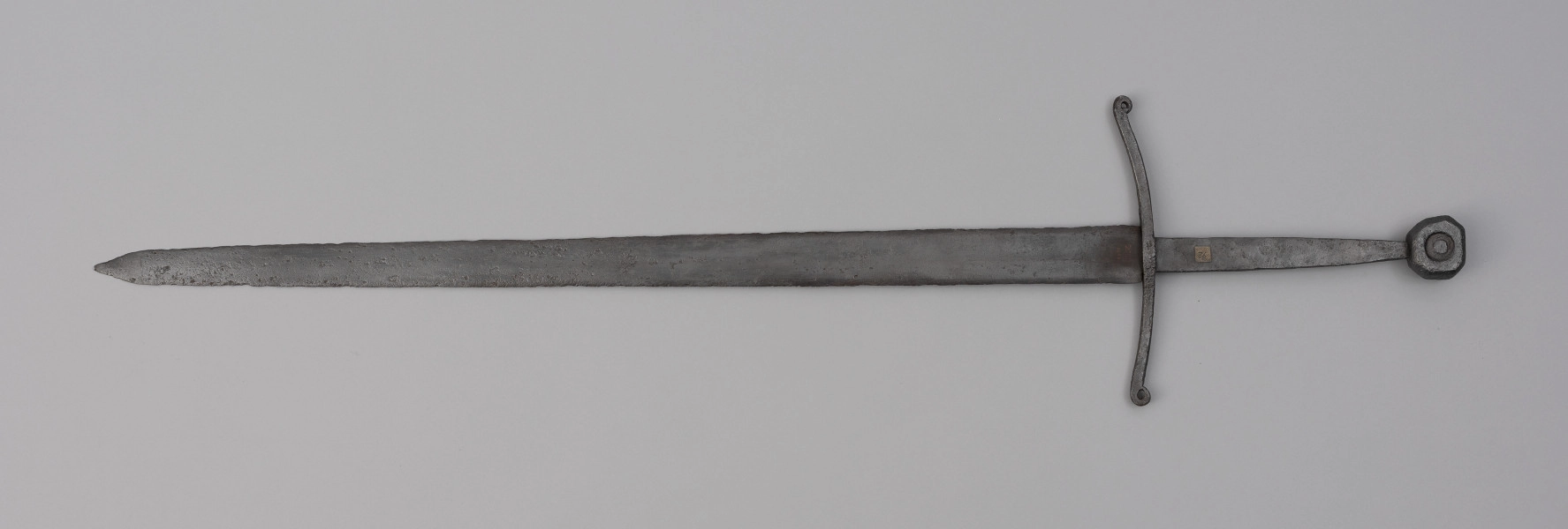 miecz typu XIIIa H2 1b (Oakeshott) - ujęcie z przodu; Miecz w typie: XIIIa, H2, 1b. Głownia o dł. 88,1 cm i szer. 4,9 cm, prosta, jednosieczna ze zbroczem, lekko zbieżna ku sztychowi. Sztych kończysty. Trzpień głowni lekko zwężający się ku końcowi. Jelec krzyżowy, lekko wygięty ku głowni, z zawiniętymi ku głowicy końcami ramion. Głowica nieregularna, ośmioboczna, z rytym dużym kołem na płaszczyznach. Znaki i zdobienia: Na głowni, złotym metalem, nieczytelny znak, dwóch okręgów, w środku których, znajdował się znak krzyża kawalerskiego, obecnie słabo czytelny. Czerwoną farbą na głowni przy nasadzie napis: ODER 1238.
