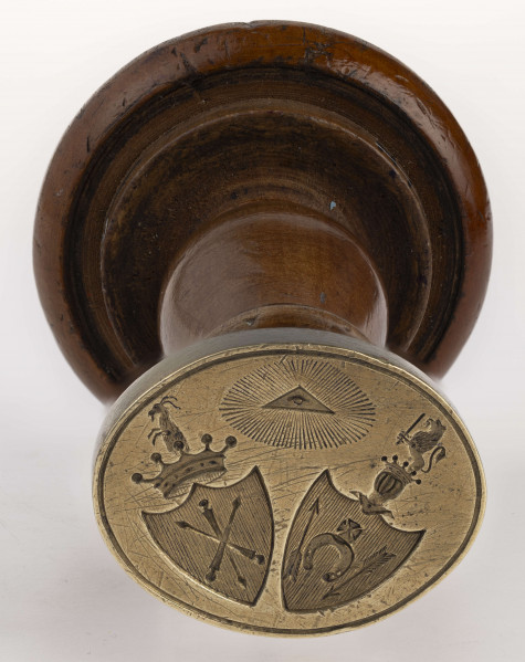 W dolnej części tłoka ukośnie umieszczone obok siebie dwie tarcze z herbami: Jelita i Łada. Herb Jelita zwienczony otwartą koroną i klejnotem; herb Łada ukoronowanym małym hełmem i klejnotem. Nad tarczami Oko Opatrzności w promienistej glorii. Obramowanie gładkim otokiem.
