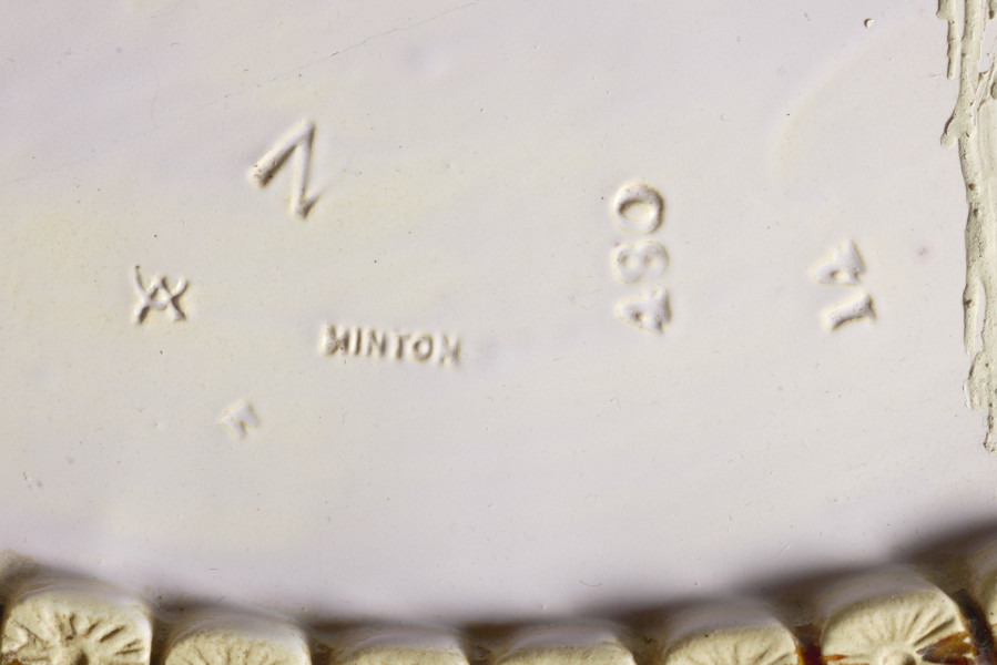 cache-pôt to duże naczynie cylindryczne, o grubych ściankach, z podstawką. Zewnętrzna powierzchnia ścianek modelowana jest na kształt wiązek łodyg bambusowych przewiązanych wstążką z kokardą. Łodygi malowane są naturalistycznie, w kolorze żółtym i brązowym. Donica i podstawka pokryte są wewnątrz polewą w kolorze liliowym. 