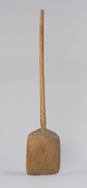 szufla do ziarna - Ujęcie z tyłu; Szufla do ziarna wykonana z jednego kawałka drewna o szerokiej i płaskiej części pracującej u dołu, której boki i górną krawędź pozostawiono grubsze. Krawędź ta przechodzi łagodnie w łukowato wygięty trzonek, zakończony prosto. Na całej powierzchni narzędzia występują ślady po drewnojadach.