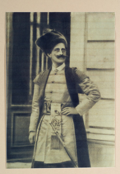 Mężczyzna o okazałych, podkręcanych wąsach, ukazany z twarzą zwróconą lekko w prawo, z lewą ręką wspartą na biodrze, sportretowany na tle architektury. Hrabia pozuje w historycznym kostiumie.