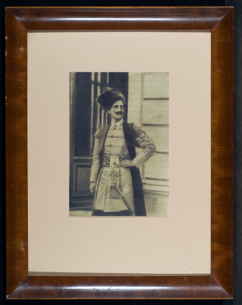 Mężczyzna o okazałych, podkręcanych wąsach, ukazany z twarzą zwróconą lekko w prawo, z lewą ręką wspartą na biodrze, sportretowany na tle architektury. Hrabia pozuje w historycznym kostiumie. 