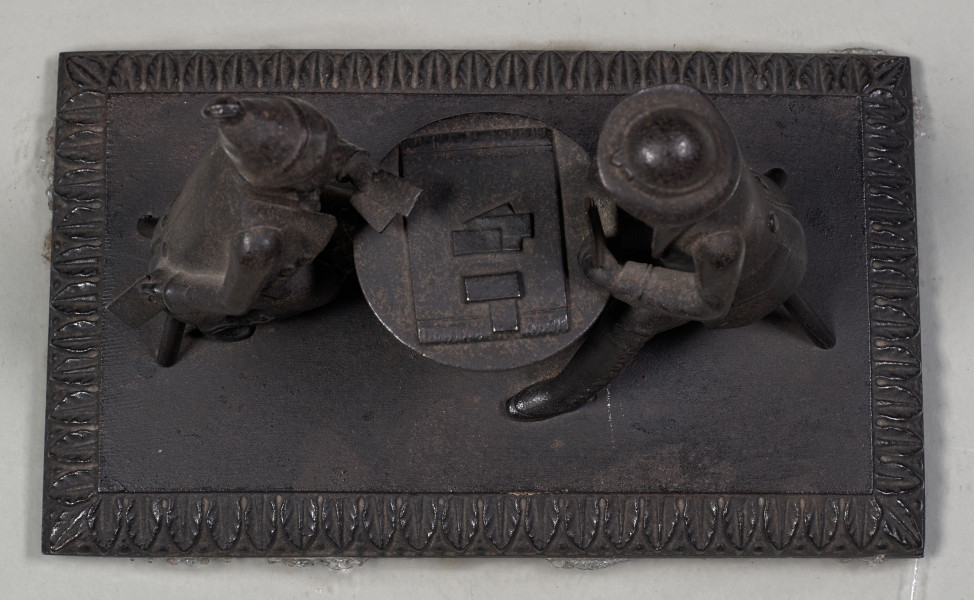 Forma przestrzenna ukazuje dwóch mężczyzn siedzących przy stoliku i grających w karty. Podstawa prostokątna ozdobiona wokół pasem ornamentalnym w motyw roślinny