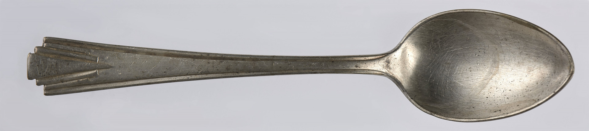 Łyżeczka deserowa wykonana ze stopu metali, pokryta cienką warstwą srebrnej powłoki (platerowana). Kształt czerpaka jest eliptyczny - silniej zwężający się w stronę zakończenia czerpaka, delikatniej w stronę trzonka. Trzonek jest płaski, lekko rozszerza się ku dołowi. Trzonek został ozdobiony oszczędnym wzorem geometrycznym (utrzymanym w stylistyce art déco). Na brzegach trzonka (na jego zakończeniu) umieszczone zostały bowiem trzy kolejne wcięcia, dzięki czemu uzyskano efekt trzech stopni. Z każdym kolejnym stopniem (w stronę krawędzi) trzonek jest coraz węższy. Efekt podkreślony jest przy pomocy płytkich rowków, które biegną skośnie od krawędzi stopnia, by zbiec się w jednym miejscu (na ok. 1/5 długości trzonka licząc od jego krawędzi). Połączenie wcięć tworzących stopnie i podkreślających je rowków pozwoliło na uzyskanie efektu nawiązującego do wachlarza. 