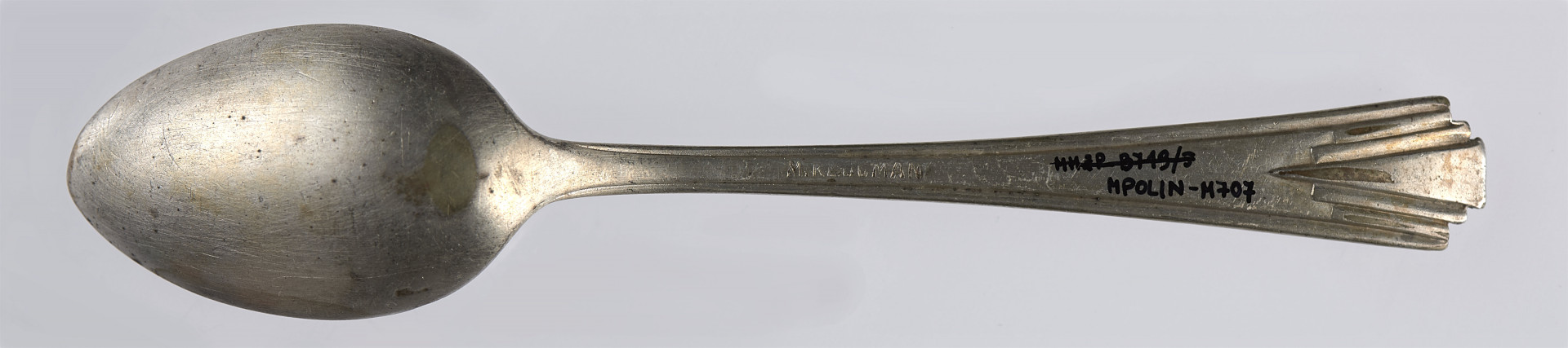 Łyżeczka deserowa wykonana ze stopu metali, pokryta cienką warstwą srebrnej powłoki (platerowana). Kształt czerpaka jest eliptyczny - silniej zwężający się w stronę zakończenia czerpaka, delikatniej w stronę trzonka. Trzonek jest płaski, lekko rozszerza się ku dołowi. Trzonek został ozdobiony oszczędnym wzorem geometrycznym (utrzymanym w stylistyce art déco). Na brzegach trzonka (na jego zakończeniu) umieszczone zostały bowiem trzy kolejne wcięcia, dzięki czemu uzyskano efekt trzech stopni. Z każdym kolejnym stopniem (w stronę krawędzi) trzonek jest coraz węższy. Efekt podkreślony jest przy pomocy płytkich rowków, które biegną skośnie od krawędzi stopnia, by zbiec się w jednym miejscu (na ok. 1/5 długości trzonka licząc od jego krawędzi). Połączenie wcięć tworzących stopnie i podkreślających je rowków pozwoliło na uzyskanie efektu nawiązującego do wachlarza. 