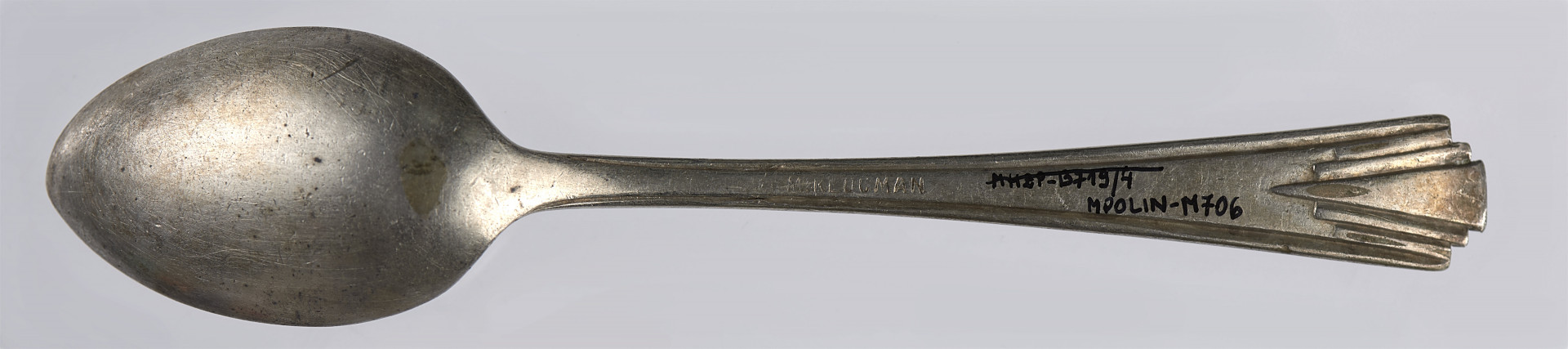 Łyżeczka deserowa wykonana ze stopu metali, pokryta cienką warstwą srebrnej powłoki (platerowana). Kształt czerpaka jest eliptyczny - silniej zwężający się w stronę zakończenia czerpaka, delikatniej w stronę trzonka. Trzonek jest płaski, lekko rozszerza się ku dołowi. Trzonek został ozdobiony oszczędnym wzorem geometrycznym (utrzymanym w stylistyce art déco). Na brzegach trzonka (na jego zakończeniu) umieszczone zostały bowiem trzy kolejne wcięcia, dzięki czemu uzyskano efekt trzech stopni. Z każdym kolejnym stopniem (w stronę krawędzi) trzonek jest coraz węższy. Efekt podkreślony jest przy pomocy płytkich rowków, które biegną skośnie od krawędzi stopnia, by zbiec się w jednym miejscu (na ok. 1/5 długości trzonka licząc od jego krawędzi). Połączenie wcięć tworzących stopnie i podkreślających je rowków pozwoliło na uzyskanie efektu nawiązującego do wachlarza. 