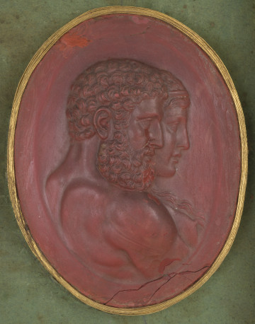 Czerwona owalna gemma ze złotym obramowaniem. Na pierwszym planie profil Herkulesa z kręconymi krótkimi włosami, brodą i wąsami, z nagim torsem. Na drugim planie profil kobiety z długimi włosami i diademem na głowie.
