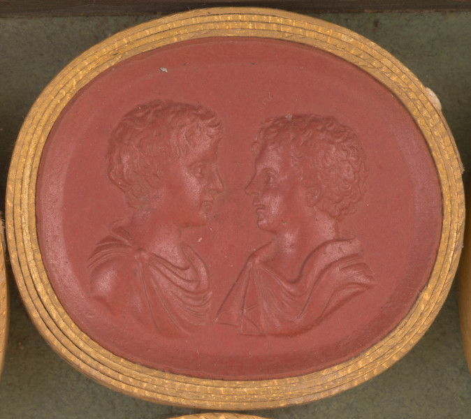 czerwona gemma, owalna pozioma, w grubym złotym obramowaniu. Popiersia dwóch chłopców zwróconych ku sobie. Prawy profil wyższego z braci, lewy - niższego, młodszego. Na ramionach młodzieńców spięte fibulami tuniki.