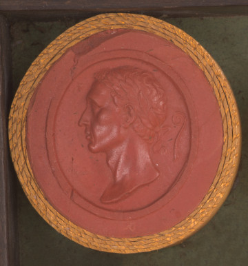 czerwona, prawie okrągła gemma, w złotym obramowaniu. Lewy profil mężczyzny o krótkich włosach, w wieńcu laurowym na głowie. Nos nieco garbaty, wydatna broda. Nad czołem gwiazdka, z tyłu głowy trąbka lituus - instrument muzyczny o długiej rurze zagiętej na kształt fajki.